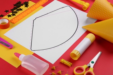 Photo of Handmade party hat template and supplies on red background