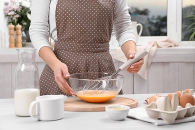 Woman whisking eggs in bowl at table indoors, closeup