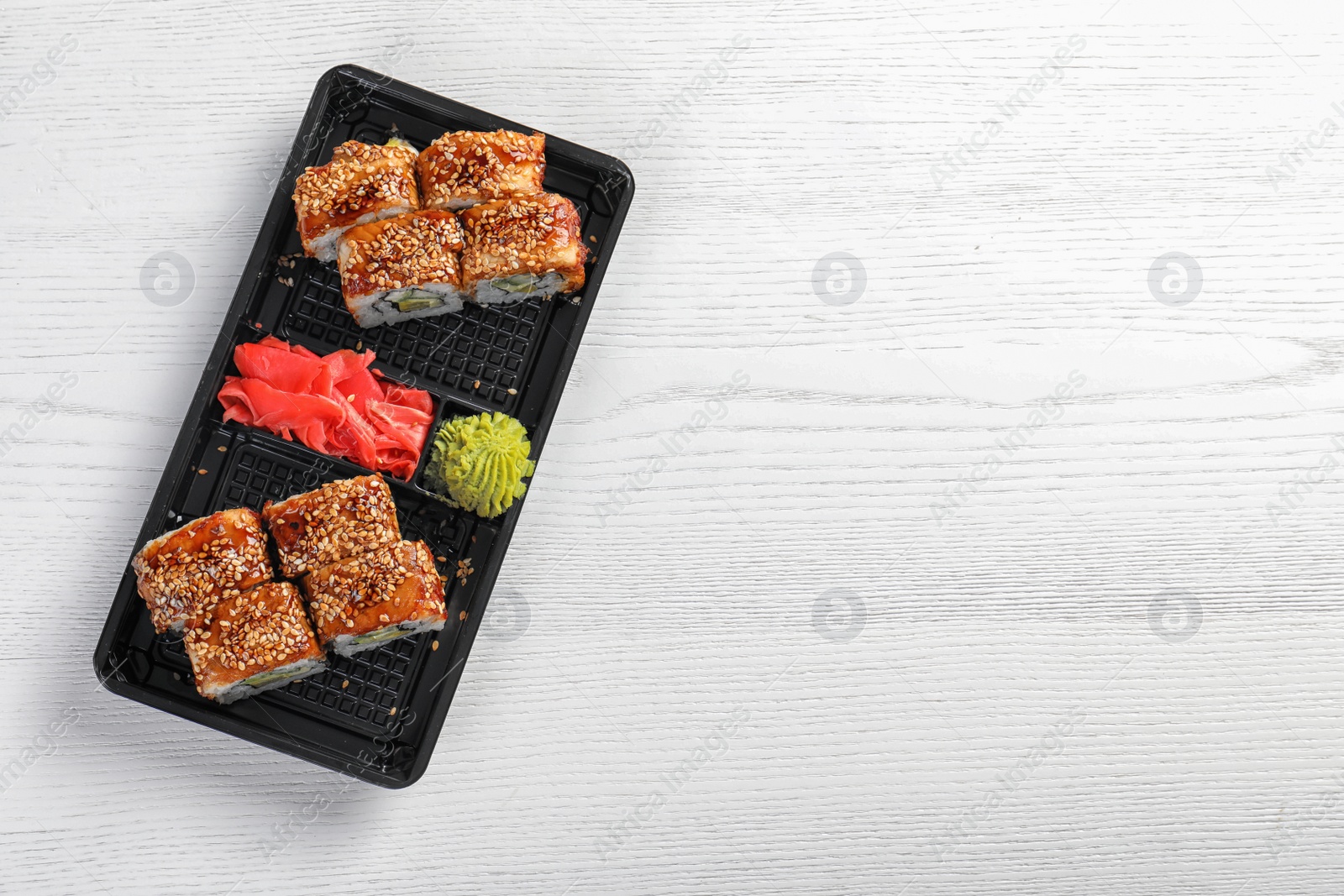 Photo of Tasty sushi rolls in box on white wooden table, top view with space for text. Food delivery