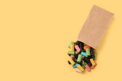 Photo of Tasty liquorice candies and paper bag on yellow background, top view. Space for text