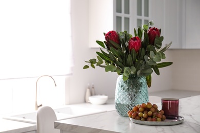 Photo of Bouquet with beautiful protea flowers on table in kitchen, space for text. Interior design