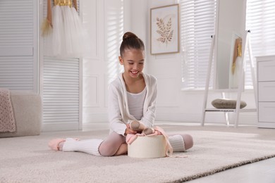 Photo of Little ballerina with new pointe shoes on floor at home