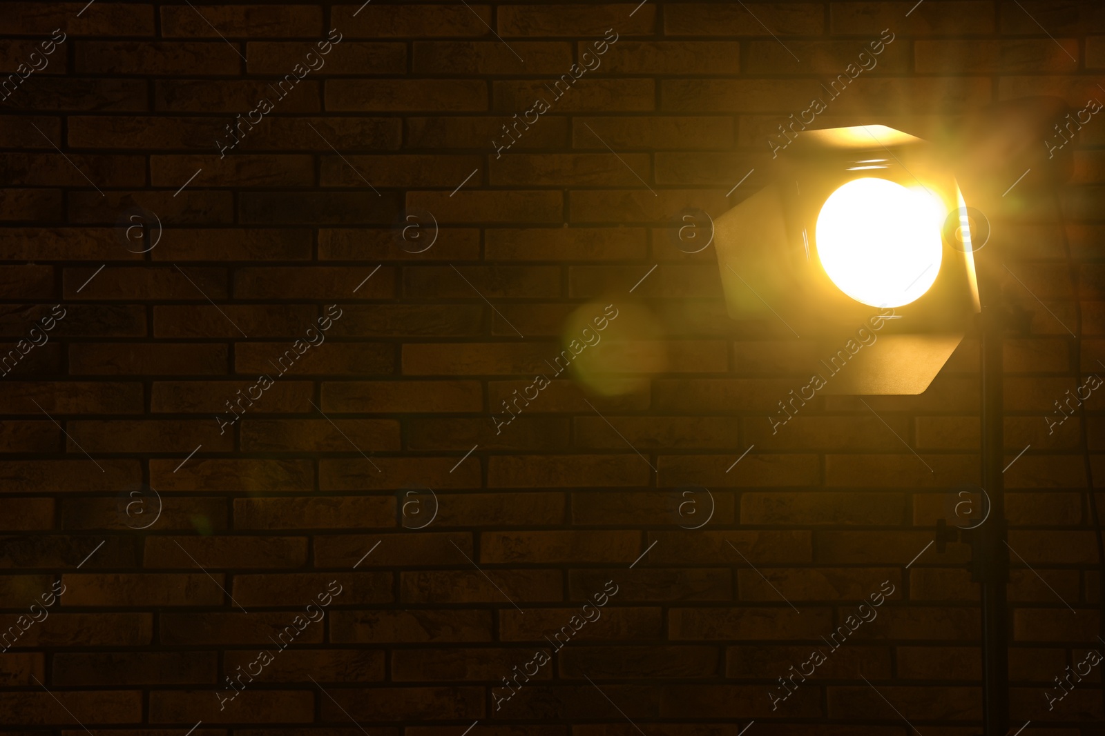 Photo of Bright yellow spotlight near brick wall in darkness, space for text