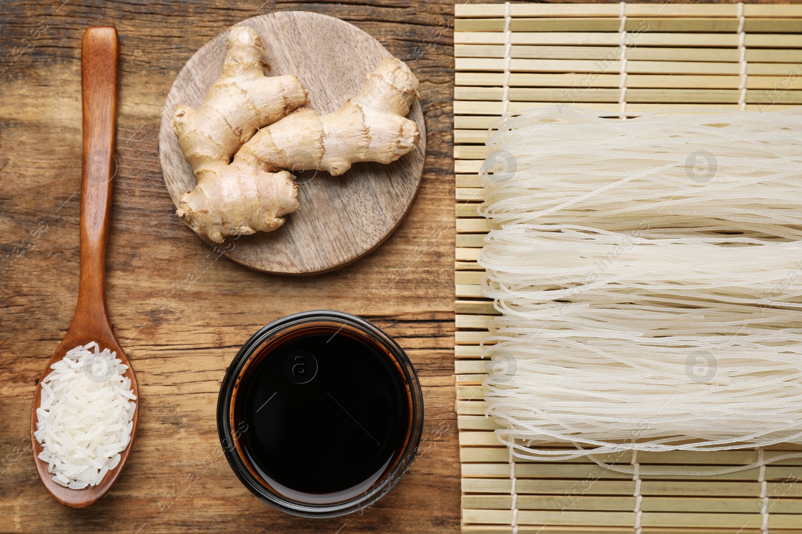 Photo of Flat lay composition with uncooked rice noodles, soy sauce and ginger on wooden table