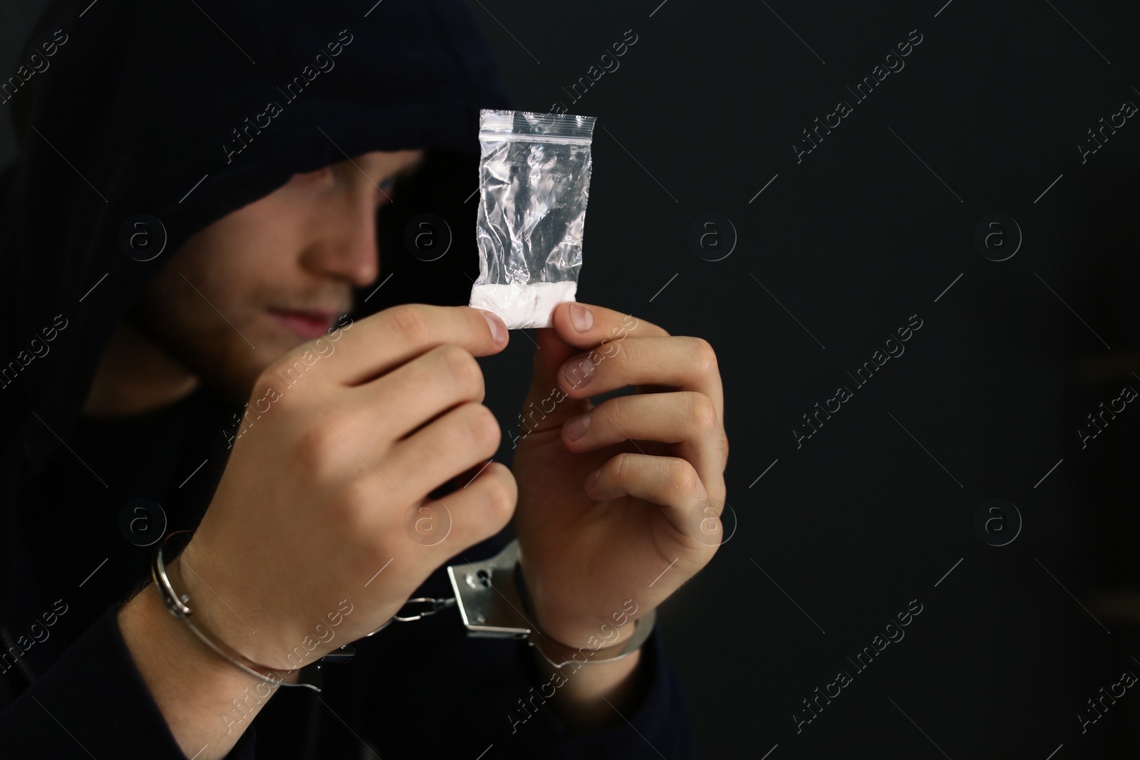 Photo of Man detained in handcuffs holding bag with drug against dark background, space for text. Criminal law