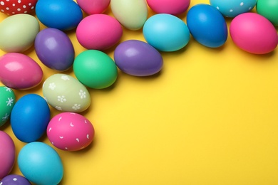 Photo of Bright painted eggs on yellow background, flat lay with space for text. Happy Easter