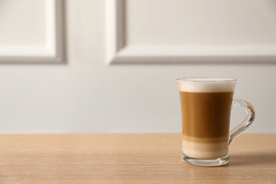 Photo of Hot coffee with milk in glass cup on wooden table. Space for text