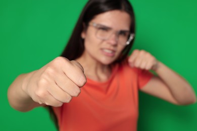 Young woman ready to fight against green background, focus on hand. Space for text