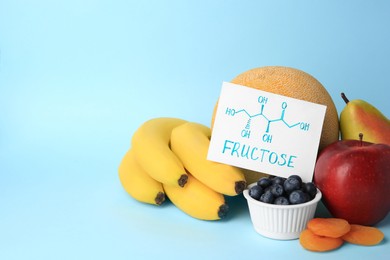 Photo of Card with word Fructose, delicious ripe fruits, blueberries and dried apricots on light blue background, space for text