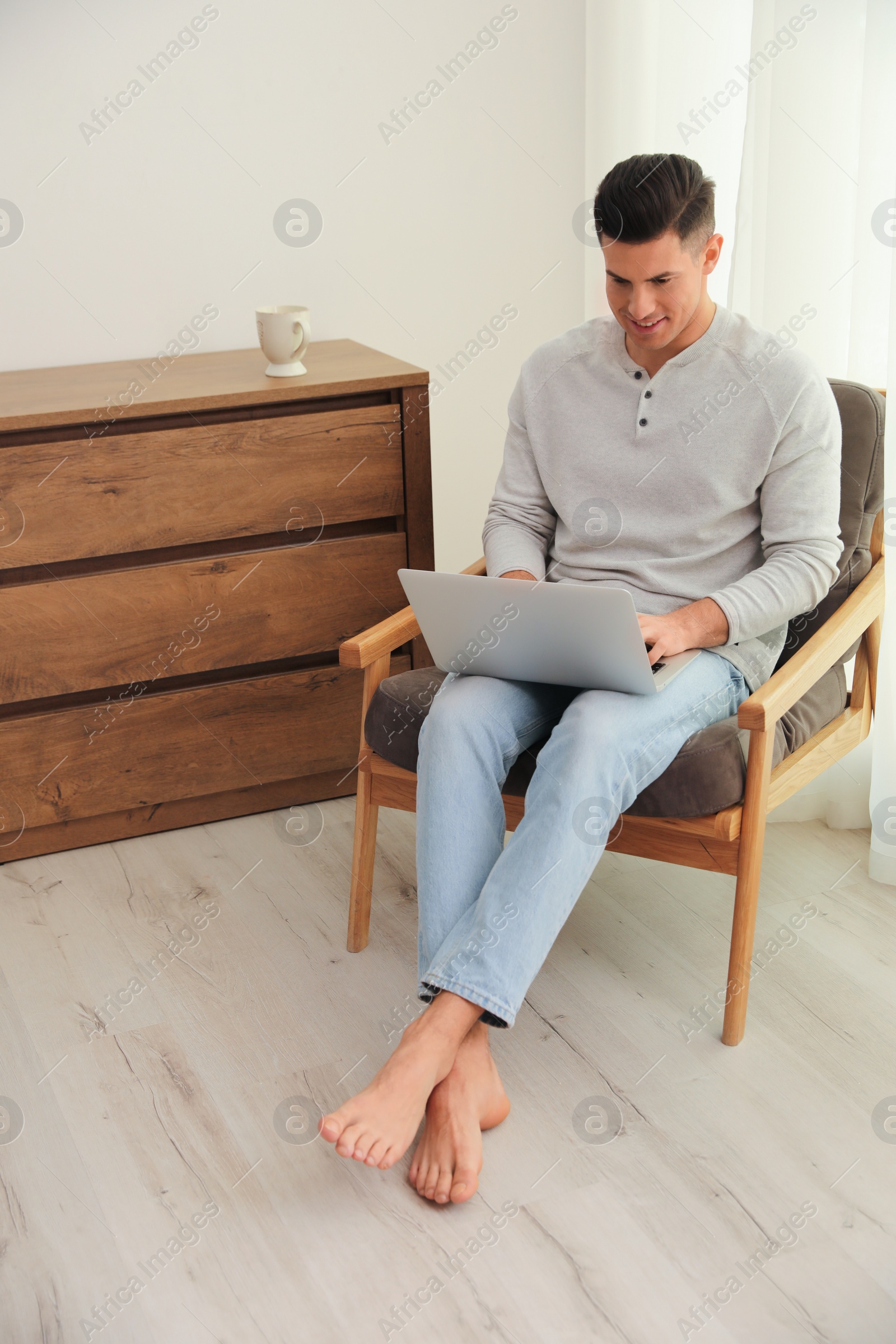 Photo of Man with laptop sitting in armchair at home. Floor heating system