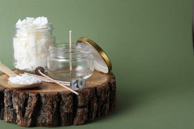 Photo of Homemade candle ingredients on wooden stump against green background, space for text