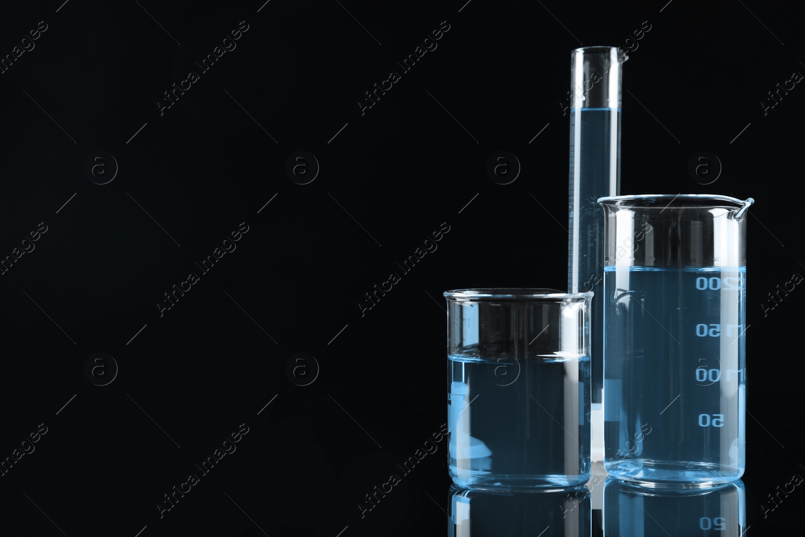 Image of Laboratory glassware with light blue liquid on black background, space for text