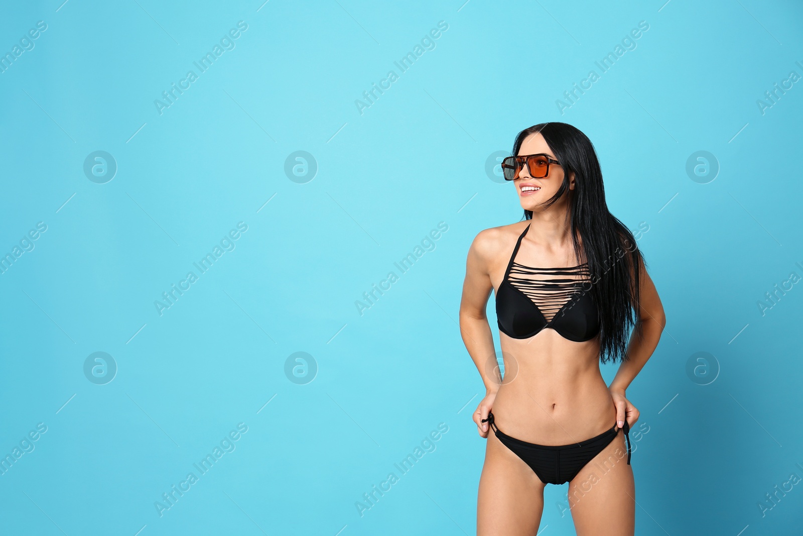 Photo of Beautiful young woman in stylish bikini with sunglasses on light blue background. Space for text