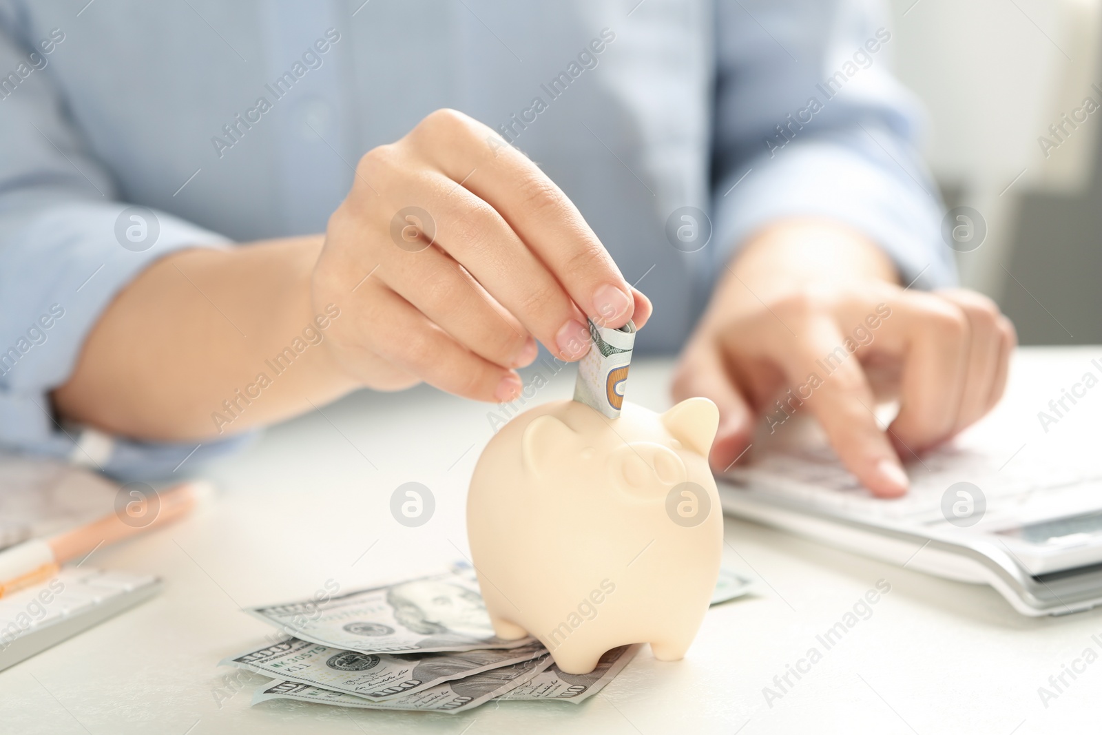 Photo of Woman putting money into piggy bank at table, closeup