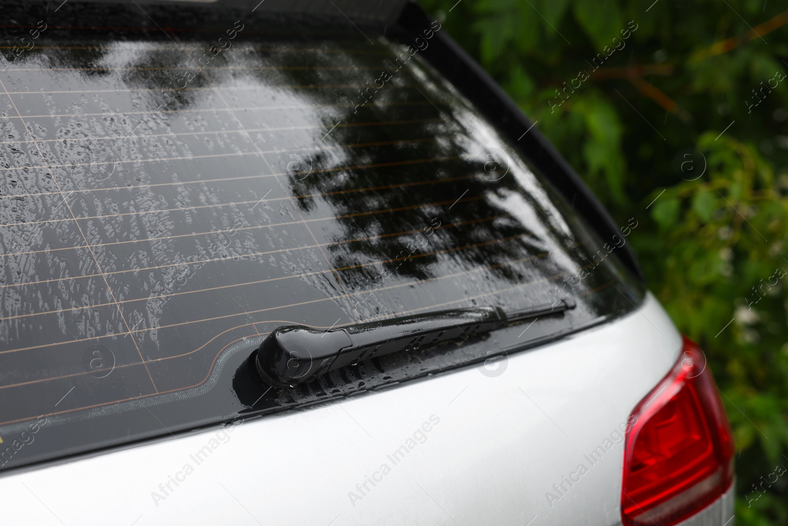 Photo of Wiper cleaning raindrops from car rear windshield outdoors