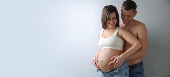 Man touching his pregnant wife's belly on light background, space for text. Banner design