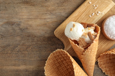 Photo of Waffle cone with ice cream, caramel and nuts on wooden table, top view. Space for text