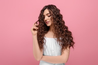 Photo of Beautiful young woman with long curly brown hair on pink background