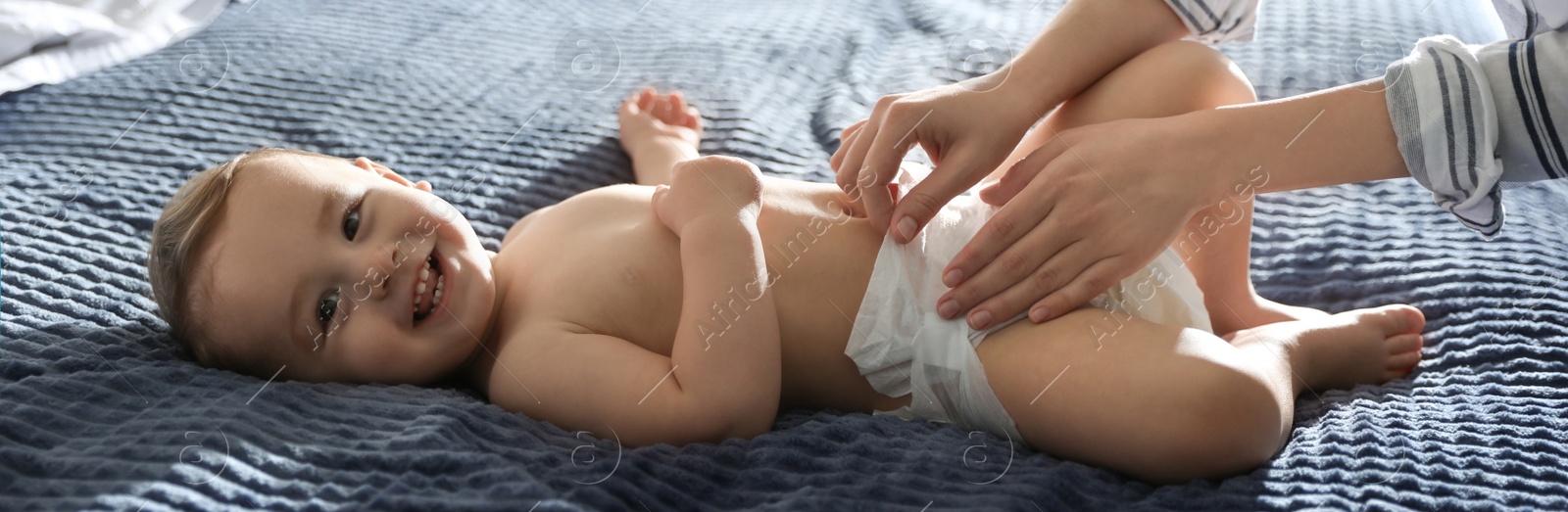 Image of Young nanny changing baby's diaper on bed at home. Banner design 