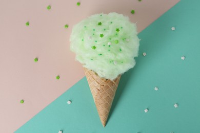 Photo of Sweet cotton candy in waffle cone on color background, top view