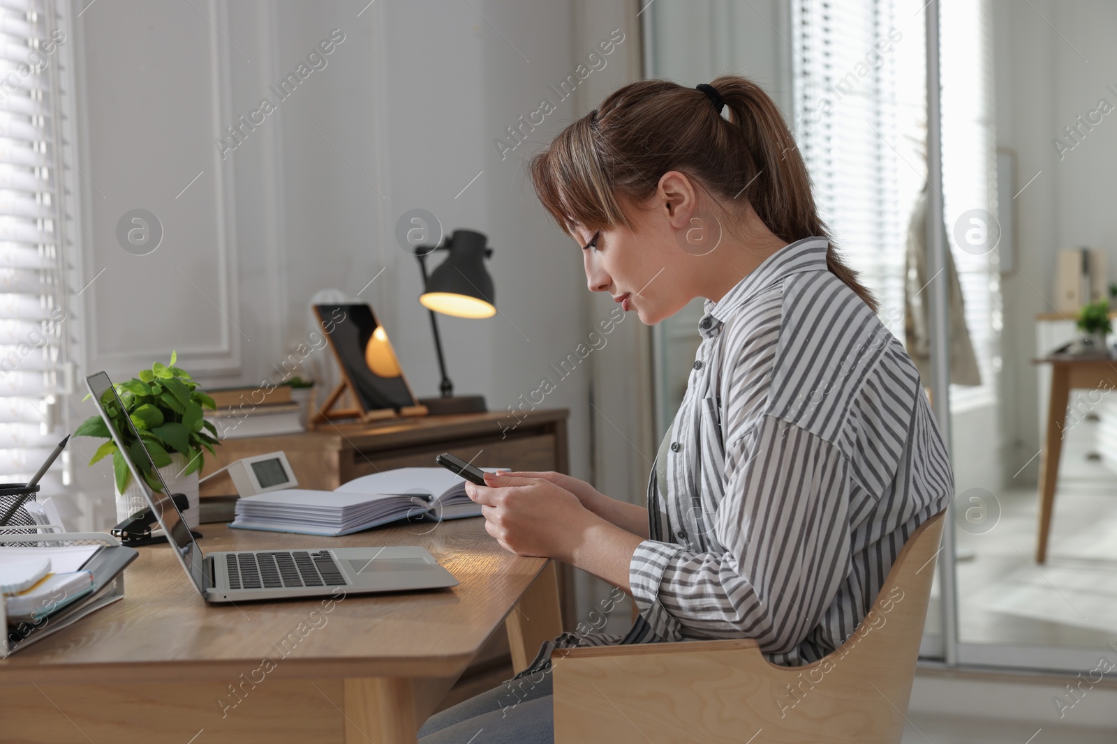 Photo of Young woman with poor posture using smartphone at table indoors