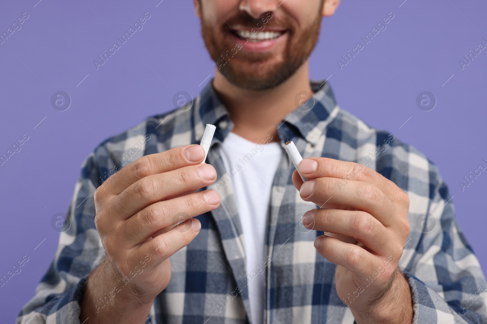 Photo of Stop smoking concept. Man holding pieces of broken cigarette on purple background, closeup