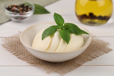 Photo of Tasty mozzarella slices and basil leaves on white wooden table, closeup