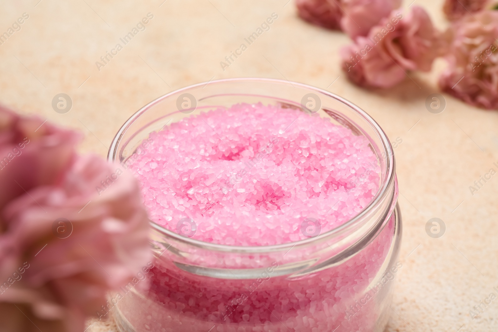 Photo of Aromatic sea salt and flowers on beige textured table, closeup