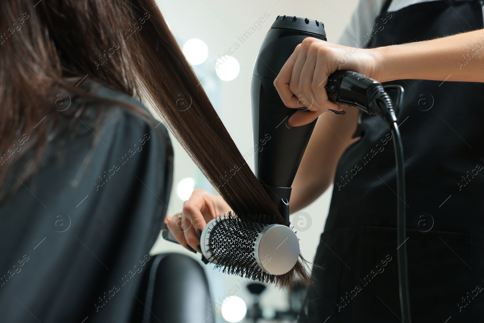 Photo of Hairdresser drying woman's hair in beauty salon, closeup