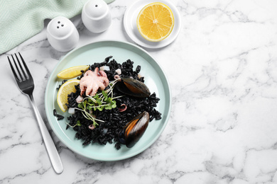 Photo of Delicious black risotto with seafood served on white marble table, flat lay. Space for text