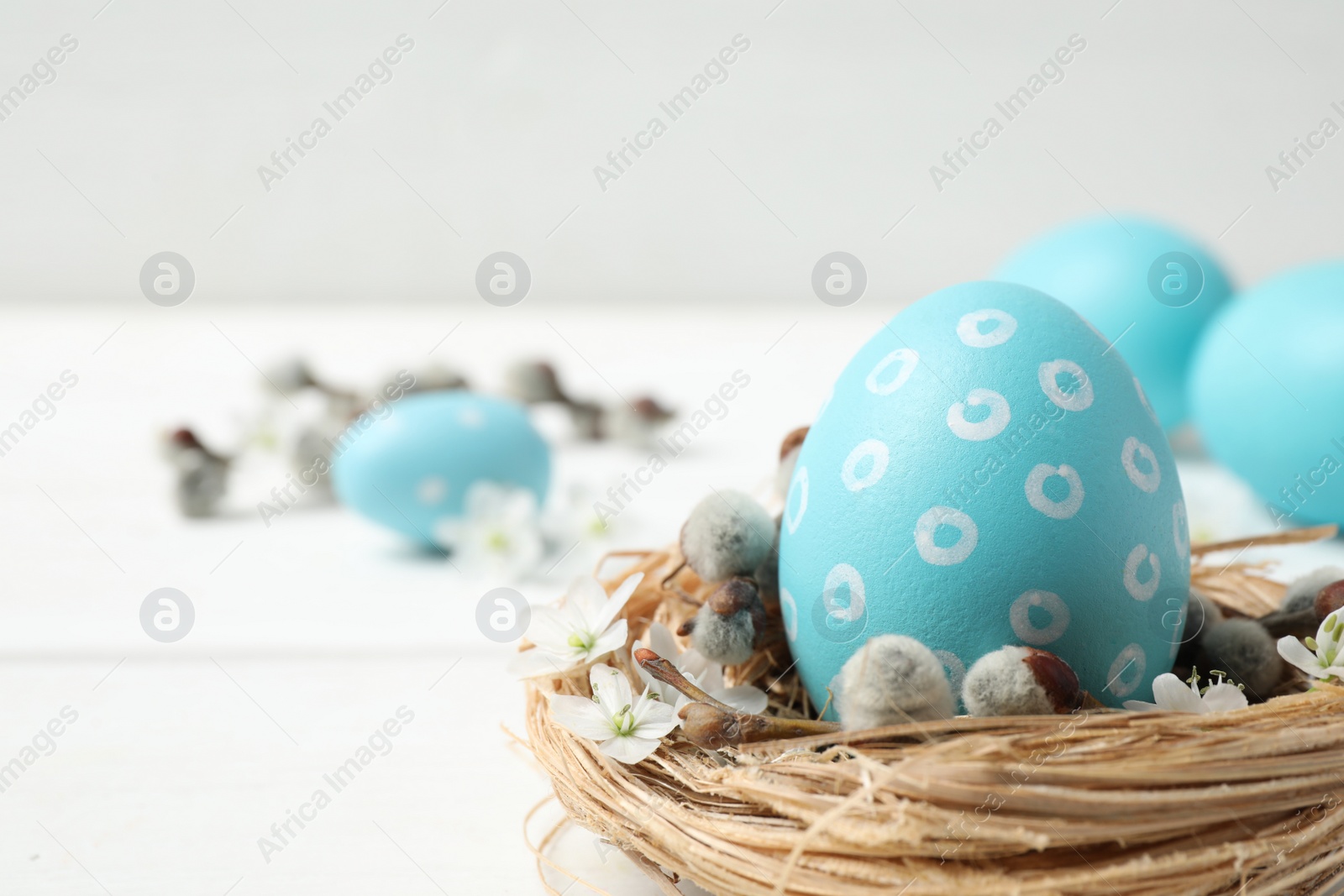 Photo of Colorful Easter egg in decorative nest on white table, closeup. Space for text