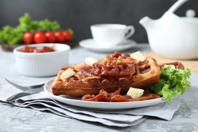 Photo of Delicious Belgium waffles served with fried bacon and butter on grey table, closeup