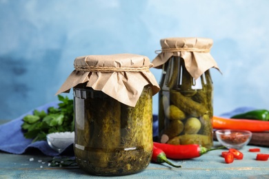 Photo of Jars with pickled cucumbers on wooden table against blue background
