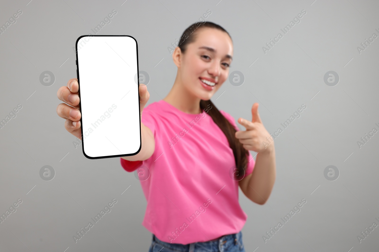 Photo of Young woman showing smartphone in hand and pointing at it on light grey background, selective focus. Mockup for design