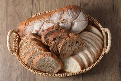 Photo of Different types of bread in wicker basket on wooden table, above view