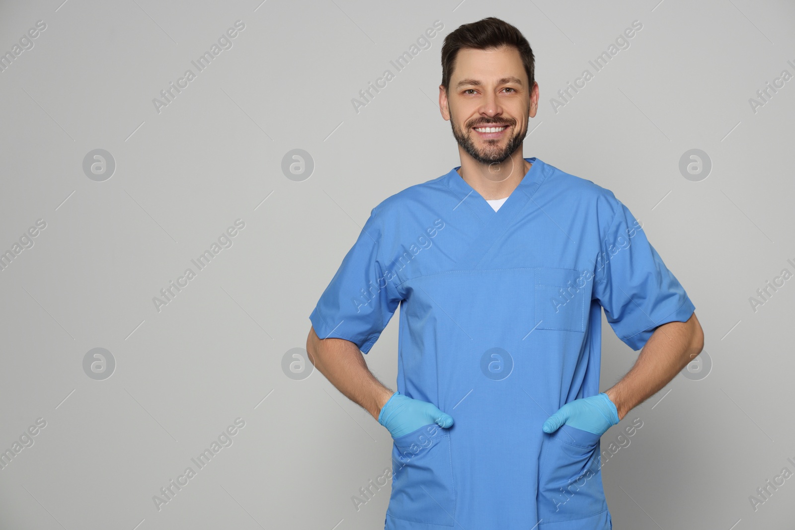 Photo of Doctor or medical assistant (male nurse) in uniform on light grey background. Space for text