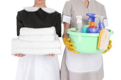 Young chambermaids with folded clean towels and detergents on white background