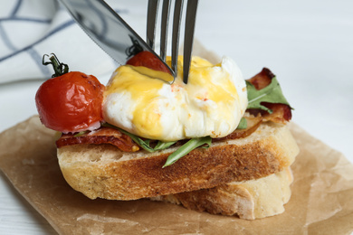Photo of Cutting tasty egg Benedict on table, closeup
