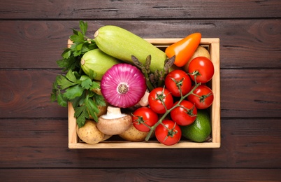 Photo of Fresh vegetables in crate on wooden table, top view