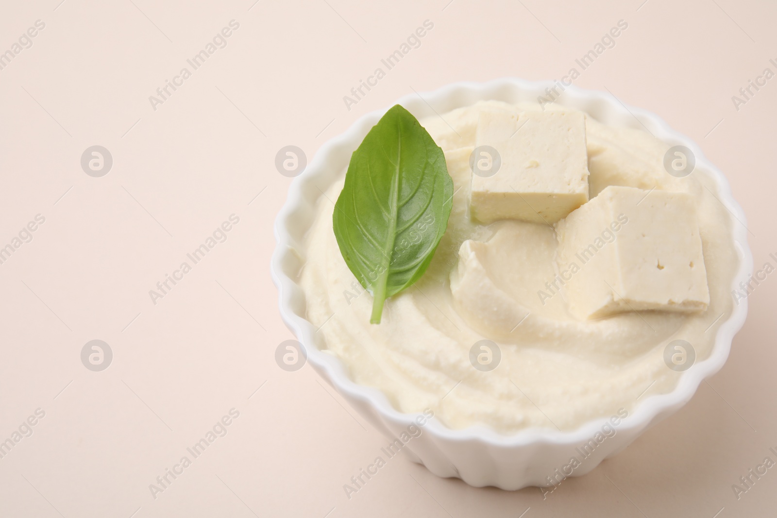 Photo of Delicious tofu sauce and basil leaf in bowl on beige background, closeup. Space for text