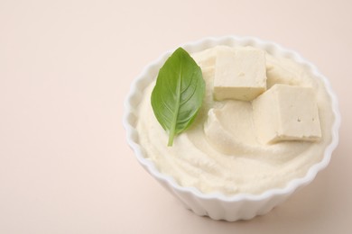 Photo of Delicious tofu sauce and basil leaf in bowl on beige background, closeup. Space for text