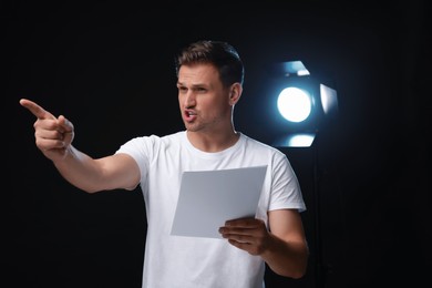 Casting call. Emotional man with script performing on black background