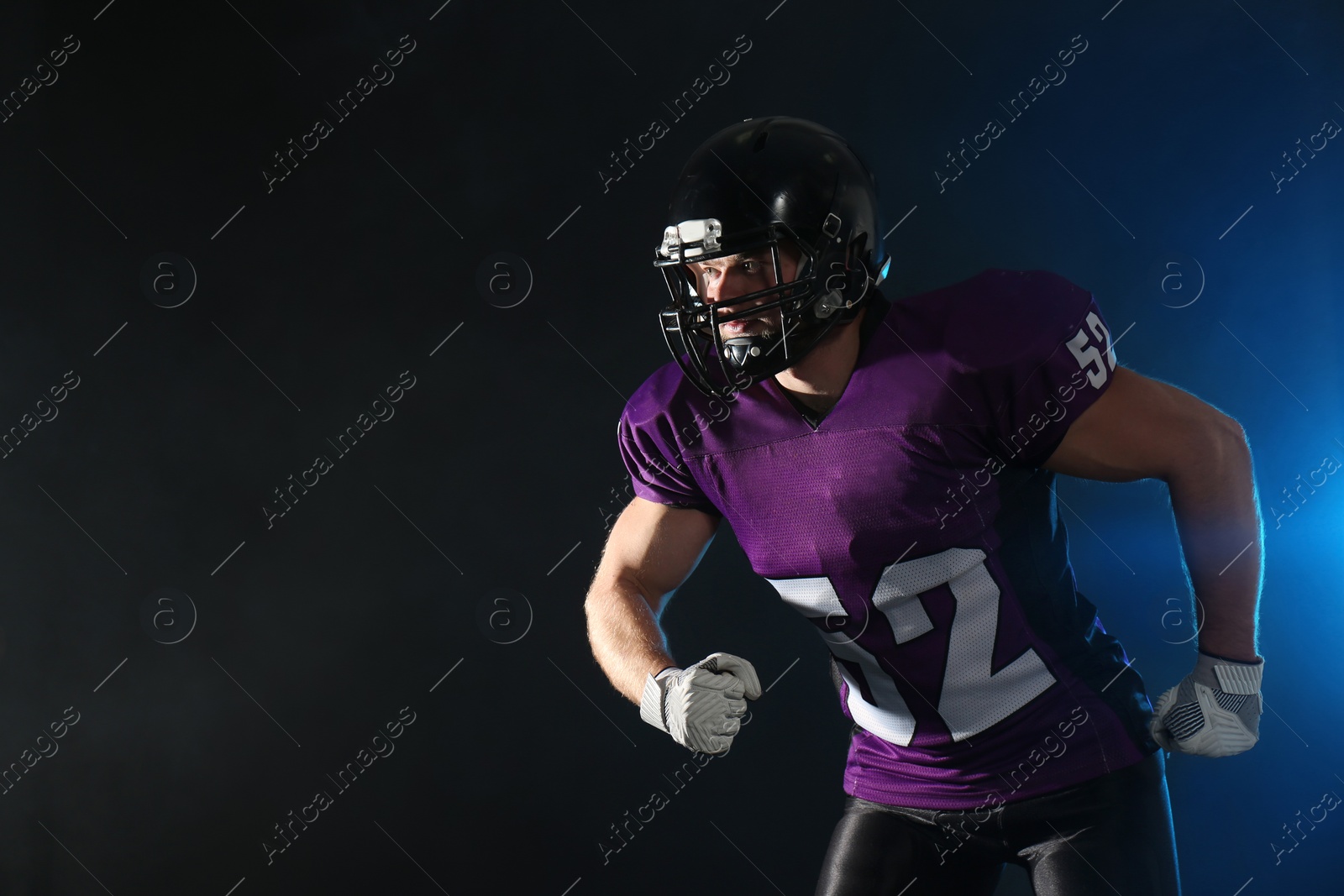 Photo of American football player wearing uniform on dark background. Space for text