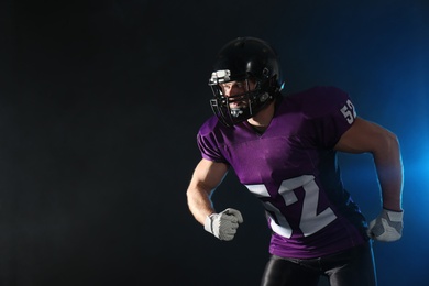 Photo of American football player wearing uniform on dark background. Space for text