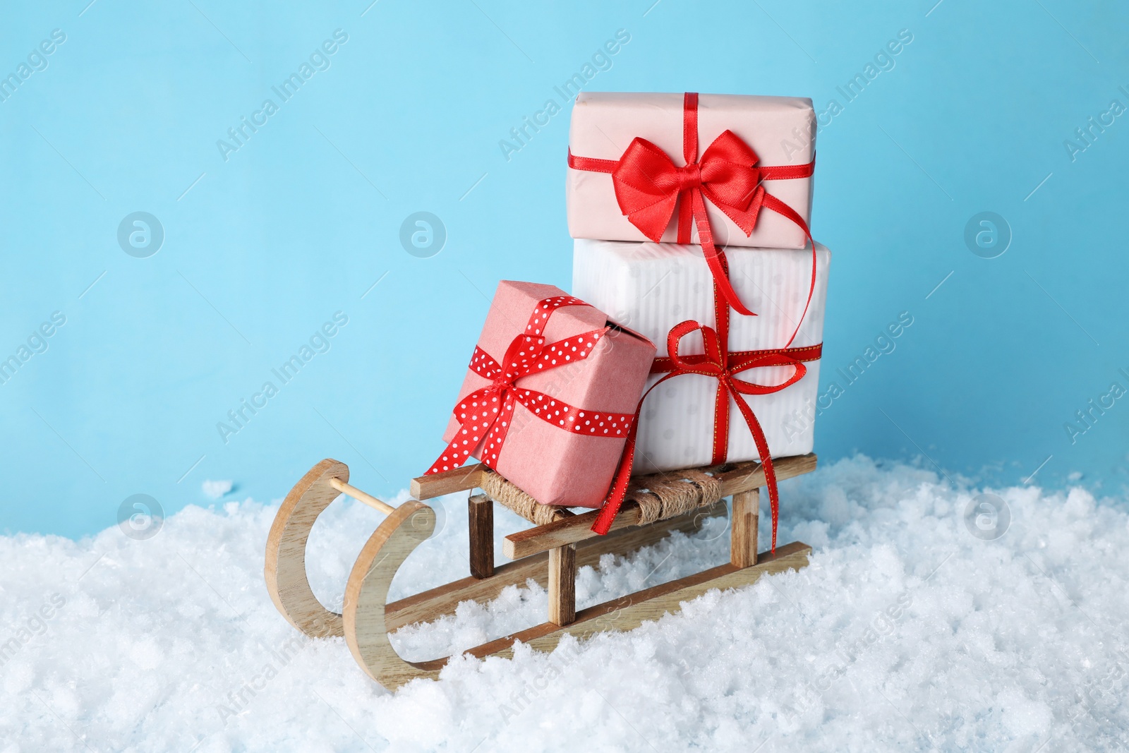 Photo of Wooden sleigh with Christmas gift boxes and artificial snow on light blue background