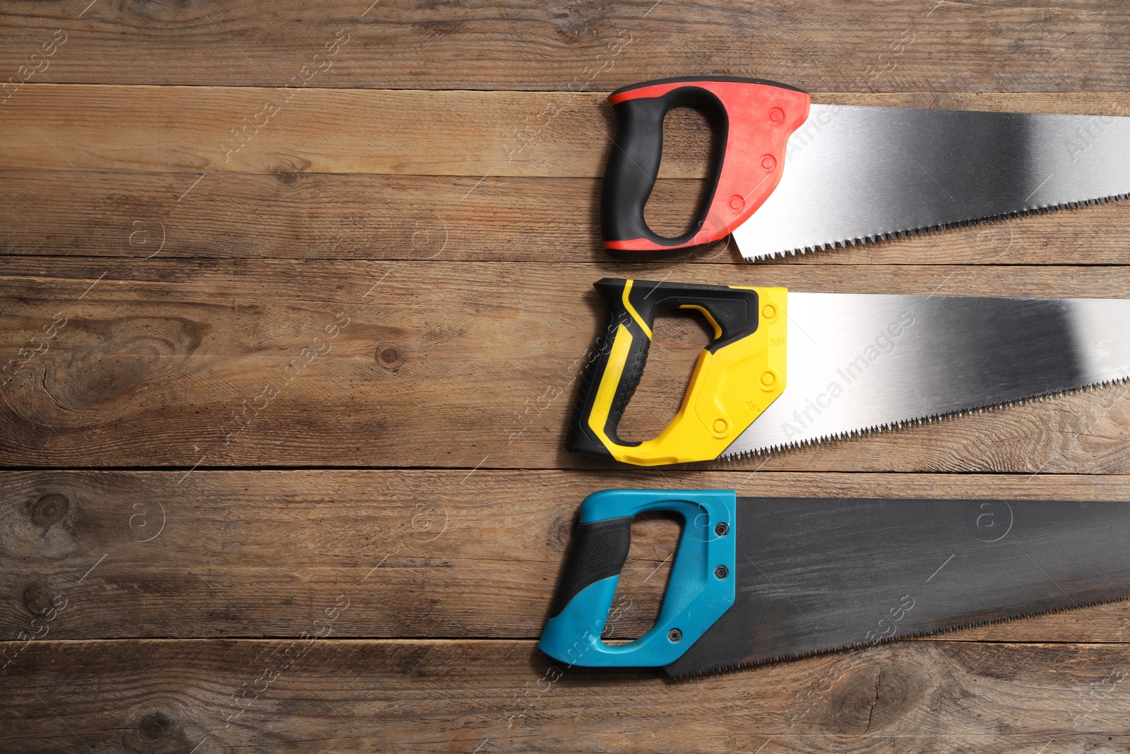 Photo of Saws with colorful handles on wooden background, flat lay. Space for text