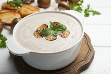 Photo of Fresh homemade mushroom soup in ceramic pot on white wooden table, closeup