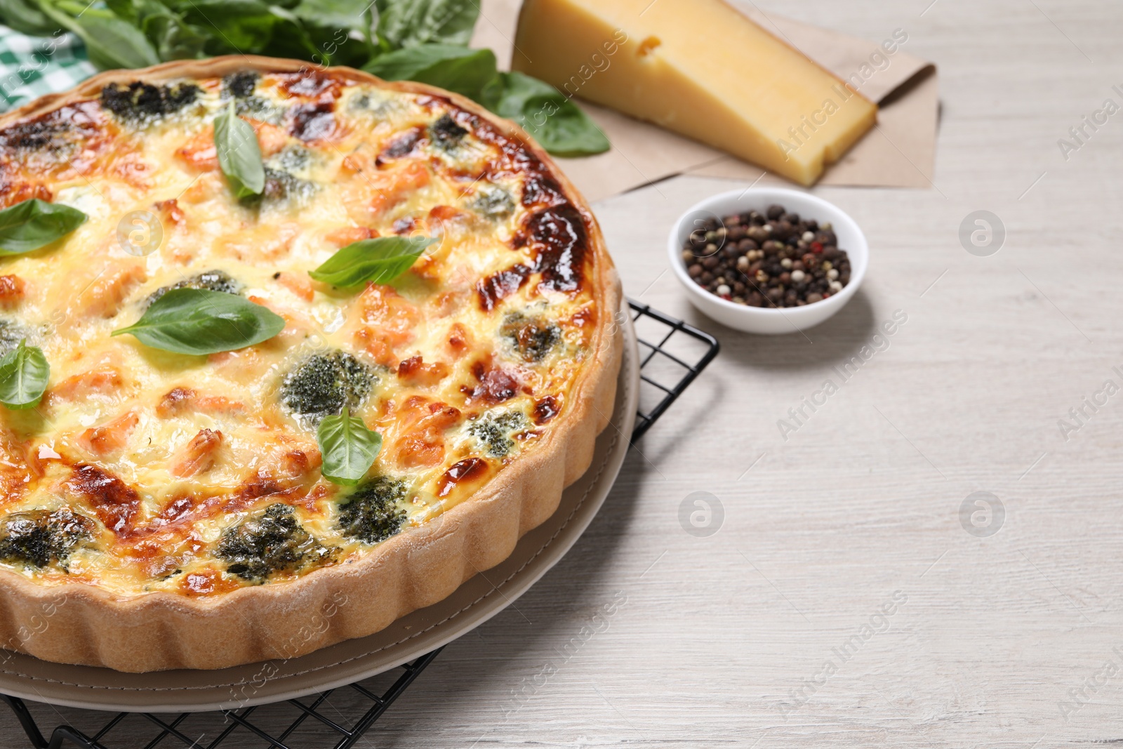 Photo of Delicious homemade quiche with salmon, broccoli and basil leaves on wooden table, space for text