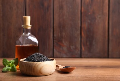 Photo of Black sesame seeds, oil and green leaf on wooden table, space for text