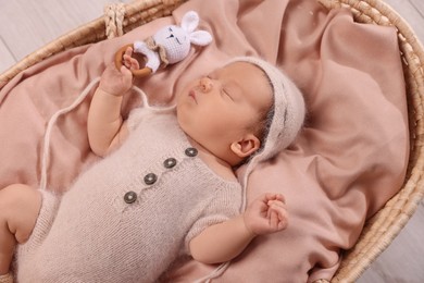Cute newborn baby sleeping with rattle in wicker crib